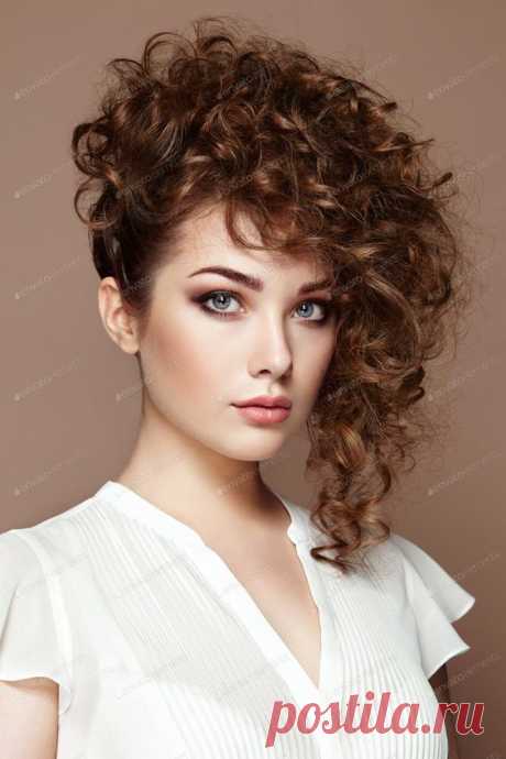 Brunette woman with curly and shiny hair. Beautiful model with wavy hairstyle. Fashion photo