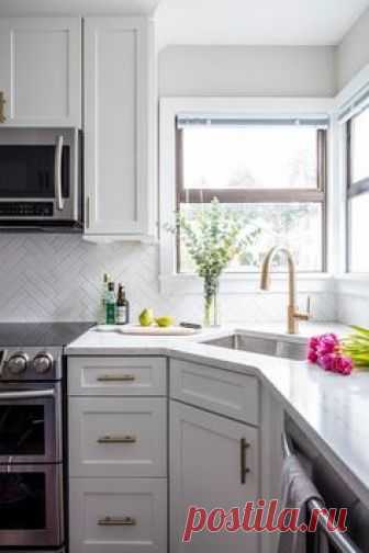 Lovely little corner kitchen sink with a brass gooseneck faucet under two windows surrounding white shaker cabinets and brass pulls.