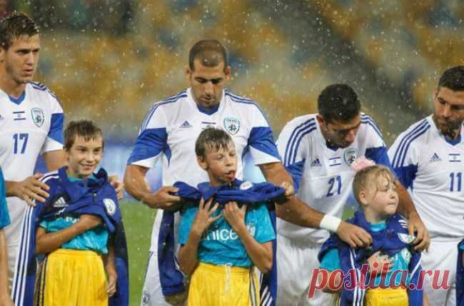 Доброта спасет мир / Украина
Израильские футболисты прикрывают украинских детей от дождя. Перед самой игрой на НСК «Олимпийский» обрушился ливень. При этом резко похолодало и стал дуть ветер. В этой ситуации команды выходили на поле. По традиции — вместе с детьми.