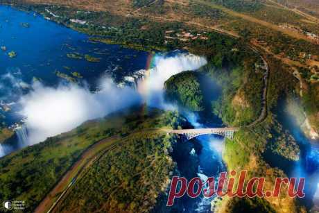 Водопад Виктория, Замбия — Зимбабве.

Между Замбией и Зимбабве вечный спор: с чьей стороны водопад красивее? Можно посмотреть с обеих: два государства соединяет мост над рекой, которая падает здесь с высоты 120 метров.

Водопад Виктория ниже Ниагарского, но мощнее и шире — он почти два километра длиной! Когда стоишь перед водопадом в облаке брызг, когда глохнешь от его рева, вся жалкая незначительность твоей жизни откроется с неоспоримой очевидностью.