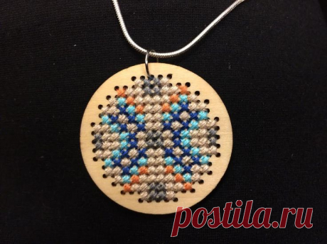 a wooden cross stitch necklace on a black background
