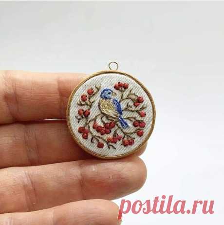 a hand holding a small embroidered ornament with red berries and a blue bird on it