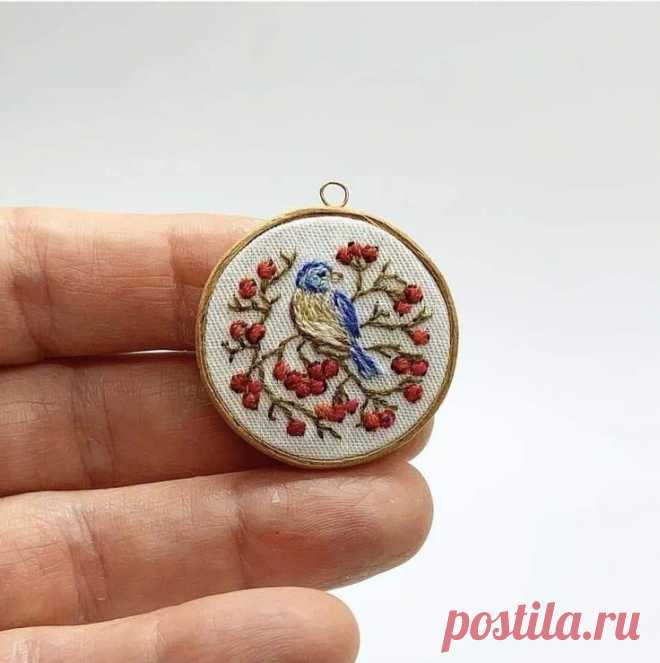 a hand holding a small embroidered ornament with red berries and a blue bird on it