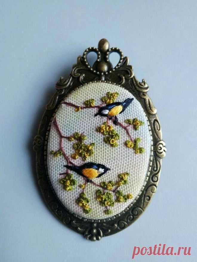 an embroidered brooch with two birds sitting on a tree branch in front of a blue background