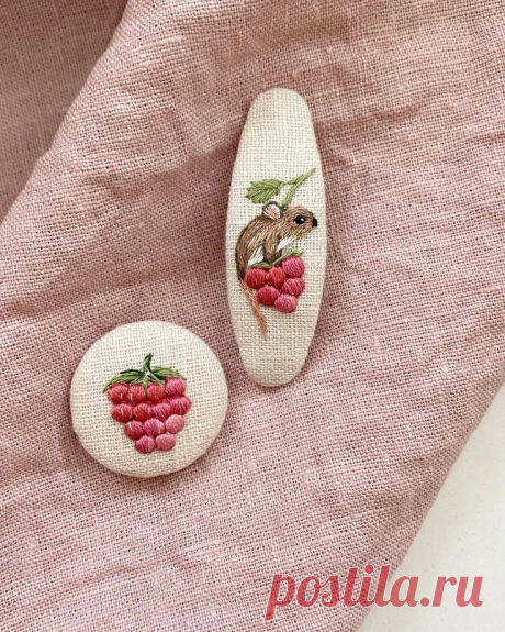 two small white rocks with red berries on them sitting on a pink cloth covered surface