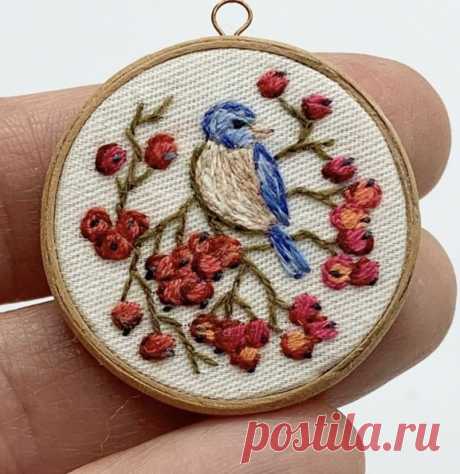 a hand is holding a small embroidered ornament with a blue bird on it