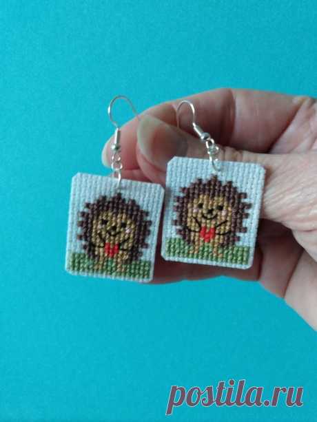 a hand holding two small square earrings with an image of a hedgehog on it