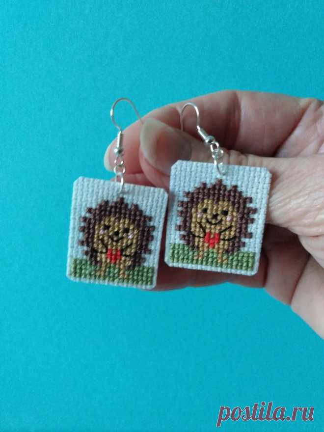 a hand holding two small square earrings with an image of a hedgehog on it