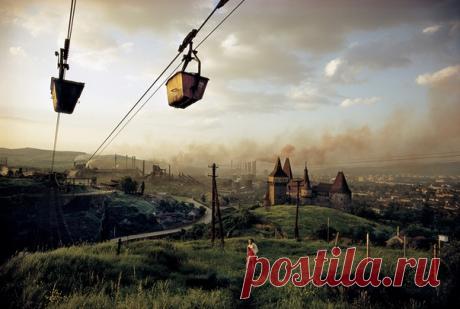 Дым из труб теснит облака в небе над румынским городом Хунедоара на фотографии, опубликованной в ноябрьском номере National Geographic за 1975 год. Здешний металлопрокатный завод, открывшийся в 1884-м, был когда-то одним из самых преуспевающих сталелитейных производств. «Всего две из недавно построенных мартеновских печей Хунедоары выплавляют больше стали, чем весь завод на предыдущем оборудовании», — говорилось в подписи к фотографии. Крах коммунизма, случившийся в Румынии в 1989 году, ударил…