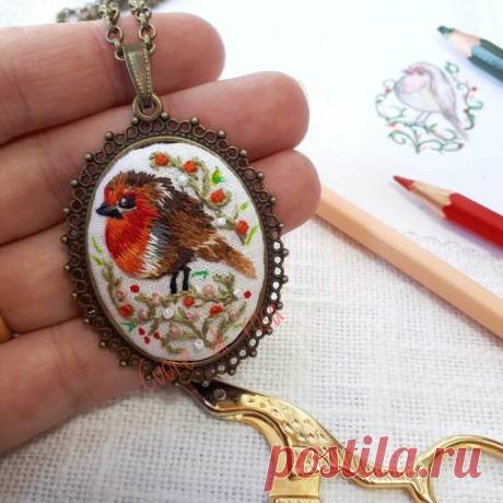 a hand holding a needle - embroidered pendant with scissors and pencils on the table