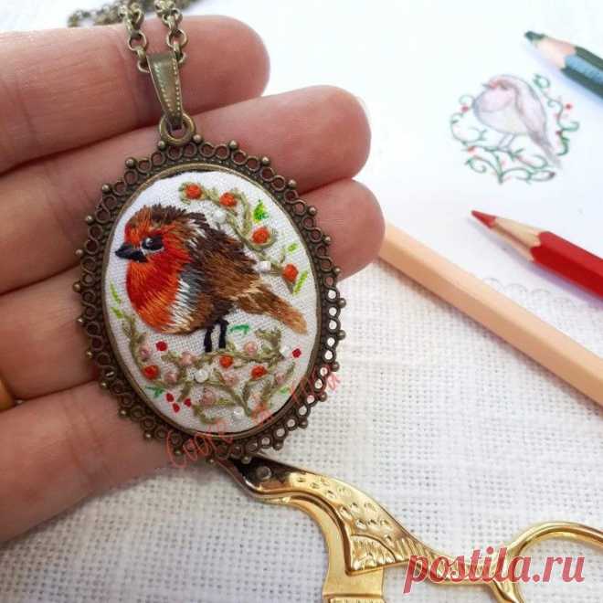 a hand holding a needle - embroidered pendant with scissors and pencils on the table