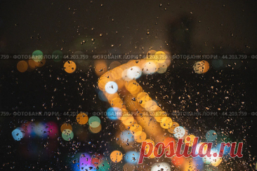 Blurred night city street lights through window glass with raindrops. Abstract dark rainy urban bokeh background. Стоковое фото, фотограф Ilaronsia / Фотобанк Лори