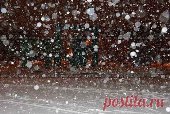 A snowstorm in progress, with snowflakes falling from the sky and covering the ground. The scene is dark and moody, with the snow creating a sense of isolation and stillness. Парк имени 50-… (2016 год) Редакционное фото, фотограф Ilaronsia / Фотобанк Лори