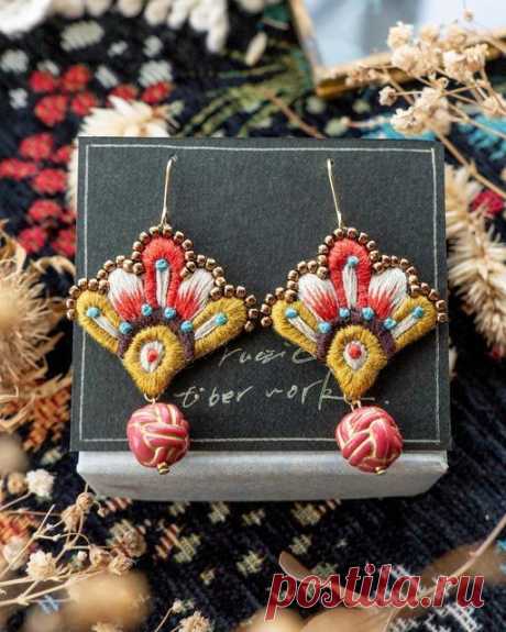 two pairs of earrings are sitting on top of a black and white box next to some dried flowers