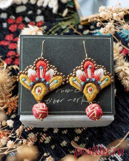 two pairs of earrings are sitting on top of a black and white box next to some dried flowers