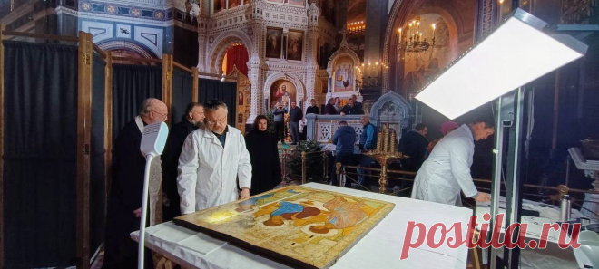 Появились фото подготовки «Троицы» к размещению в Храме Христа Спасителя. Источник РБК рассказал, как с иконы снимали профилактические заклейки, которые на нее ранее нанесли реставраторы. По его словам, на представленных фотографиях видно, что процесс проходил в «полевых условиях» — на «козлах» и доске