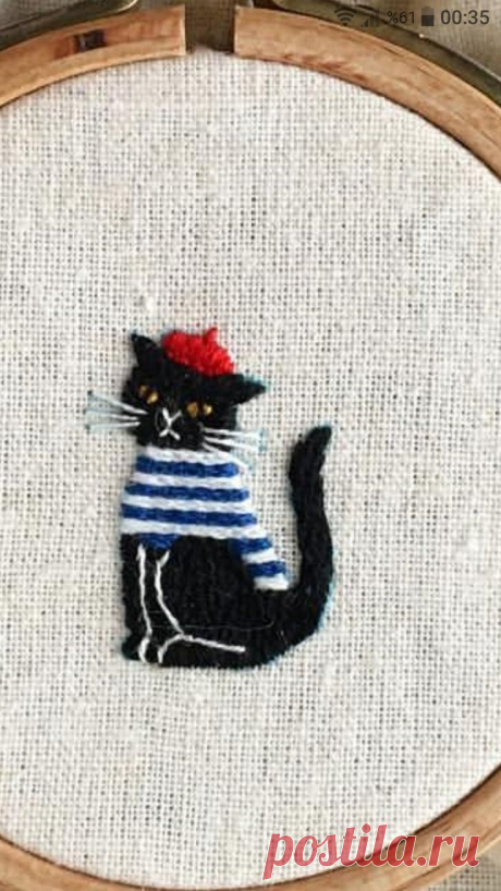 a black cat with a red hat and striped shirt is sitting in front of an embroidery hoop