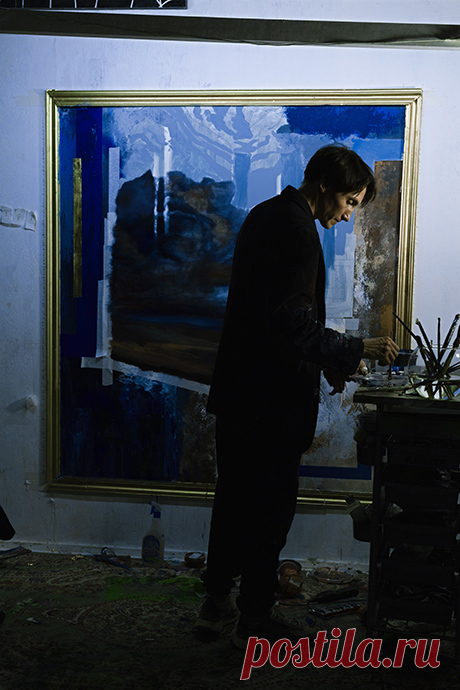 Художник Antonio Lebedef в студии работает над новой картиной в стиле глитчсюрреализм. На фото он сосредоточенно подбирает кисти, погружая их в стеклянный сосуд с водой, в то время как за его спиной рождается полотно, наполненное глубокими синими оттенками. Lebedef соединяет живопись и цифровые мотивы, исследуя хаос информационного мира и превращая его в визуальные образы. Его уникальный стиль — это смелый синтез glitch-эстетики и сюрреализма, формирующий новое направление современного искусства