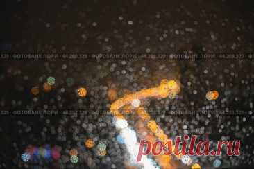 Blurred night city lights through window glass with raindrops. Abstract dark rainy urban bokeh background. Стоковое фото, фотограф Ilaronsia / Фотобанк Лори