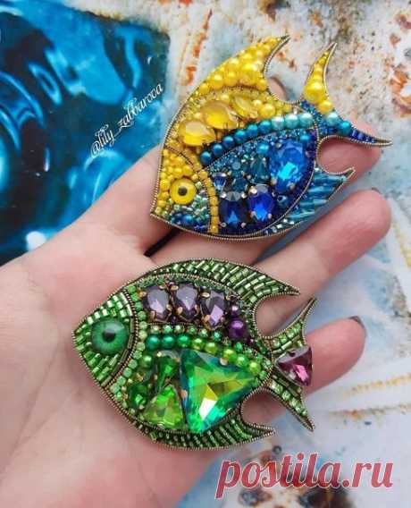 two colorful fish brooches sitting on top of each other's palm hand