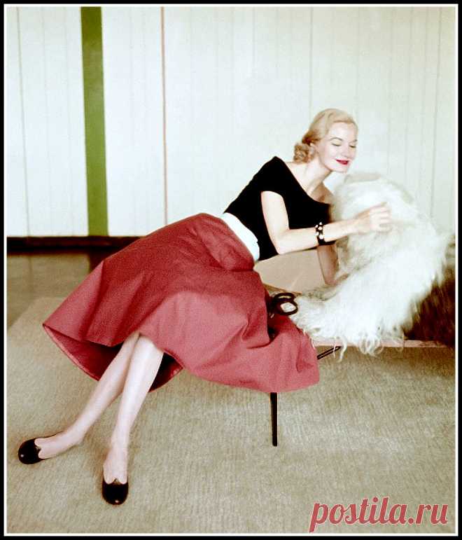 Sunny Harnett in a red canvas skirt and black jersey top is petting a white wooly dog, photo by Richard Rutledge, Vogue 1951