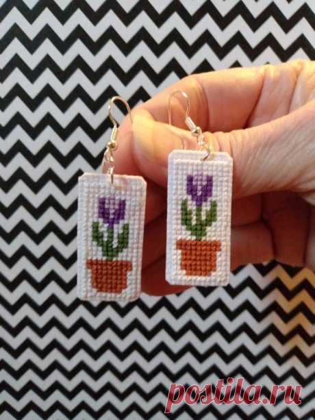 a hand holding two small earrings with flowers on them
