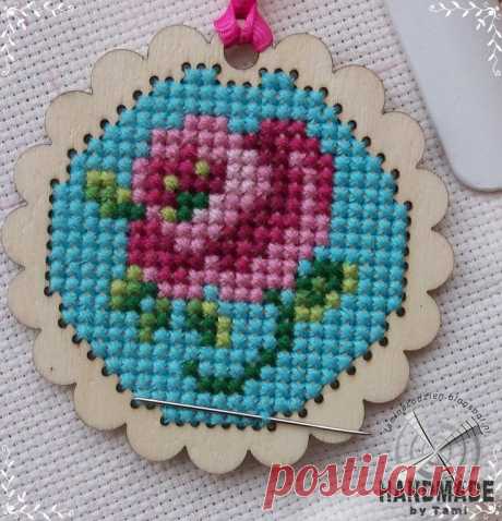 a cross stitch ornament with a pink flower in the center on a white background