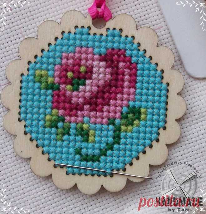 a cross stitch ornament with a pink flower in the center on a white background