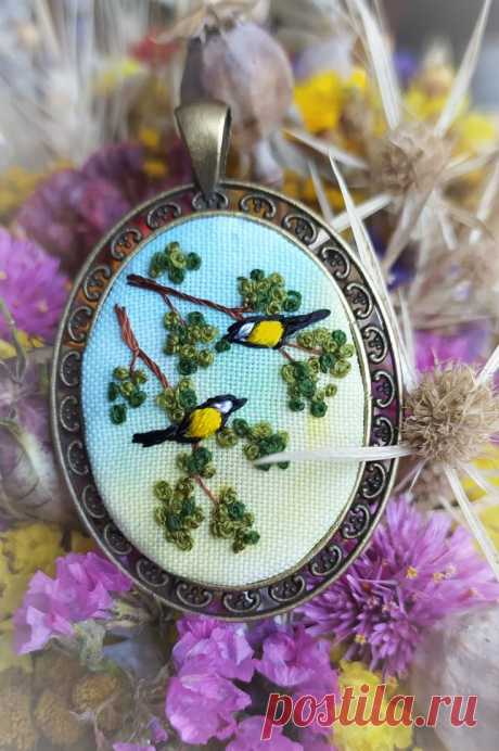 a close up of a pendant with birds on it and flowers in the foreground
