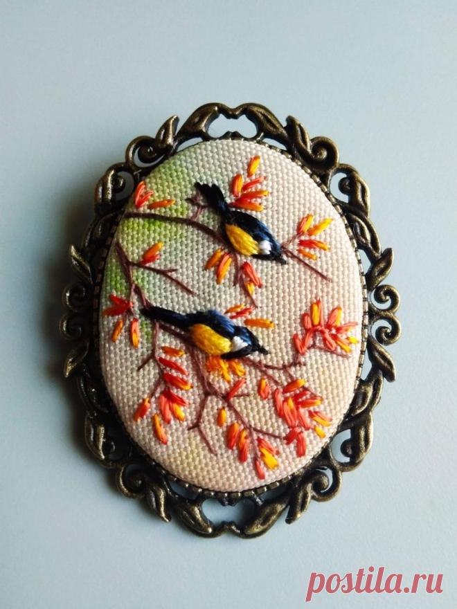 a brooch with two birds sitting on a tree branch and orange flowers in the center