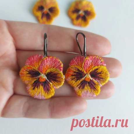 a pair of earrings with flowers on them sitting in the palm of someone's hand