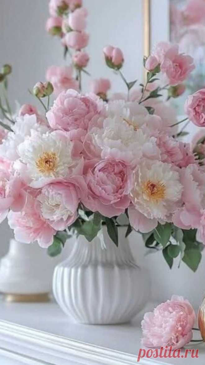 pink and white flowers are in a vase on a mantle next to an ornate mirror