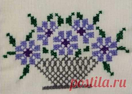 a cross stitch pattern with purple and green flowers in a basket on a white background