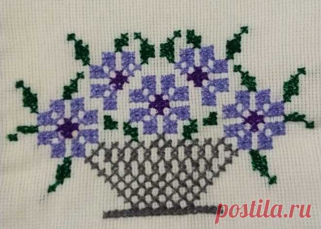 a cross stitch pattern with purple and green flowers in a basket on a white background