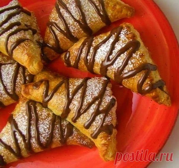 СЛОЙКИ С БАНАНОМ И НУТЕЛЛОЙ Ингредиенты:-Слоеное тесто 500 гр; -Банан 2 шт; -Ореховая паста Nutella 100 гр; -Яйца куриные 1 шт.  Приготовление:Готовое слоеное тесто (2 упаковки по 250 гр) разморозить при комнатной температуре. Банан очистить от кожуры, нарезать ломтиками. Нутеллу набрать в кондитерский шприц. Тесто разрезать на одинаковые квадраты. В верхний угол каждого квадрата положить ломтик банана. Сделать ре...