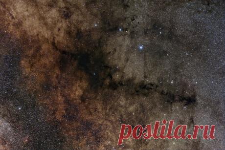 Темная туманность в центре называется Курительная Трубка. Темные облака при некоторой доли фантазии можно посчитать дымом, поднимающимся от курительной трубки. Они состоят из пыли, поглощающей свет от фоновых звезд. По облакам можно отследить путь к туманности около звезды ρ Змееносца, которая находится в верхней части снимка. На этой изображения обнаруживаются несколько типов туманностей: красные эмиссионные, голубые отражательные и темные поглощающие / Интересный космос