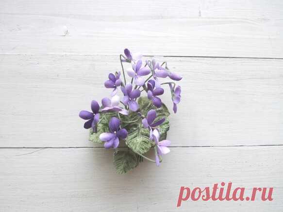 布の花　うす紫すみれのコサージュ　1 濃淡をつけたうす紫のすみれの花をこぼれるようにまとめたコサージュです。花は綿サテンを使用、少し毛羽立っています。葉はつやと毛足のあるシール布地を使い、大小の葉っぱが伸びています。タテ付けタイプです。タテに着けるよう想定してコサージュピンを付けてあります大きさ　　全長　タテ　約10㎝×　ヨコ　約8㎝（茎を含む）　　　　　クリアボックス付き。　　　　　　※　布の花は繊細な作りのものですので、お取り扱いには十分ご注意ください。※　水濡れや過度の湿気は型崩れや色落ちの原因になりますので　　ご使用や保管の際はお気をつけください。※　ご覧の画面上と実物では色が異なって見える場合があります。　　ご不明な点がありましたら、お問い合わせください。