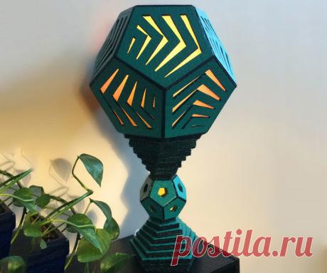 Use some scrap cardboard and a few easy to find supplies to create a decorative, geometric table lamp made of pentagons and dodecahedrons. Add a color changing LED bulb for a relaxing mood or nightlight.