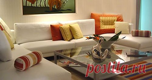 Дизайнеры украсили эту гостиную в современном стиле. В интерьере гостиной разноцветный ковёр сочетается с цветастыми подушками и картиной на стене выполненой в таком же дизайне. Прекрасные орнаменты на стеклянном столе посередине комнаты делают это помещение ещё более элегантным.