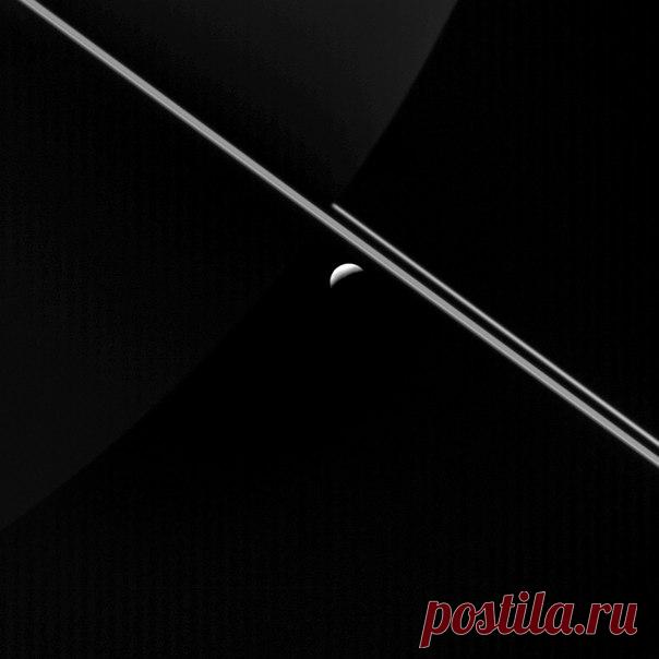 Маленький спутник Сатурна Энцелад на фоне колец планеты гиганта. На снимке также заметен полумесяц самого Сатурна освещенный отраженным светом от колец / Интересный космос