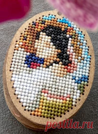 a wooden box with a cross - stitch pattern on it and a pink flower in the background