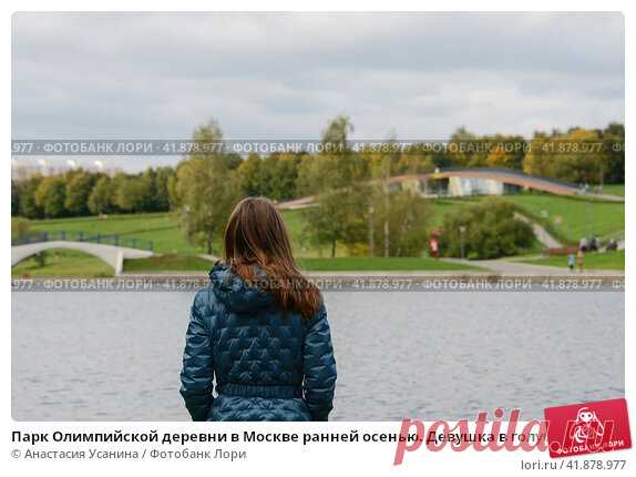 Парк Олимпийской деревни в Москве ранней осенью. Девушка в голубой куртке около пруда на фоне зелёного парка и серого неба. Стоковое фото, фотограф Анастасия Усанина / Фотобанк Лори