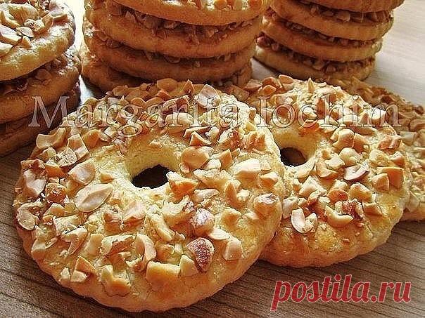 Песочные кольца с орехами

Тесто: 
250 г сливоч. масла (холодного) - порезать кусочками 
150 г сахара 
1 яйцo (среднее) 
1 п. ванил. сахара (8 г) 
1 ч. л. с горкой разрыхлителя (5 г) 
2,5 ст. муки (400 г) - просеять 

Дополнительно: 
1 ст. жареного арахиса (160 г) - порубить не мелко ножом 

Для смазывания: 
1 желток + 2 ст. л. молока - перемешать вилочкой 

В чашку выкладываем масло, сахар, яйцо, ванил. сахар и разрыхлитель - слегка перемешиваем.
Постепенно подсыпая муку,...