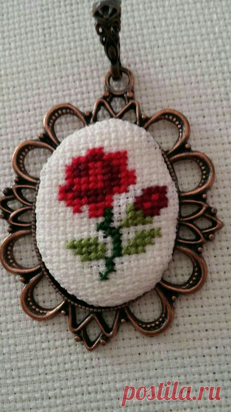 a cross stitched red flower on a white background is hanging from a metal frame