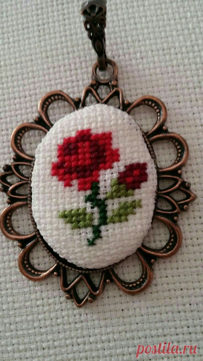 a cross stitched red flower on a white background is hanging from a metal frame