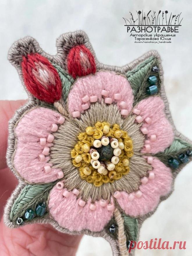 a hand is holding a flower brooch with beading on it's center