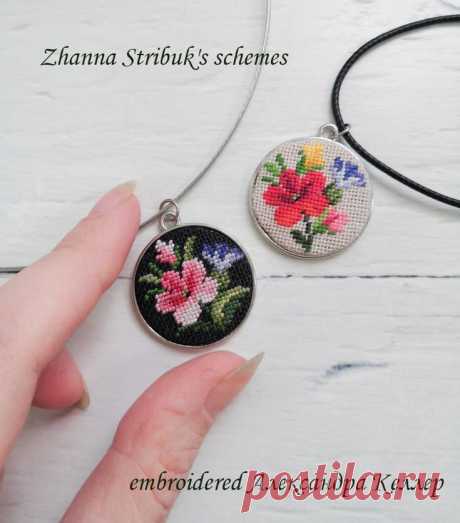 a hand is holding two pendants with flowers on them