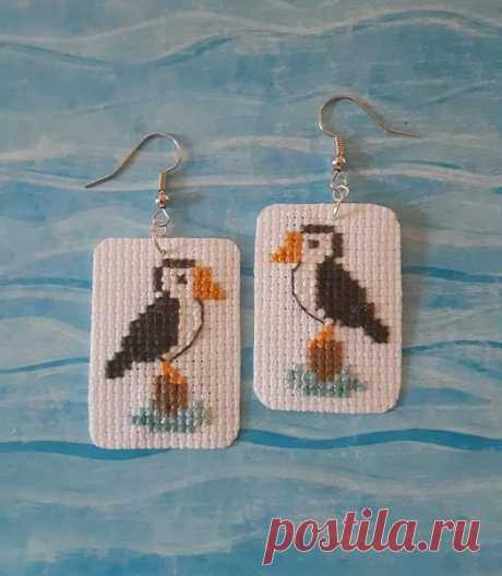 a pair of needled earrings featuring a puffy bird on a white square with blue water in the background