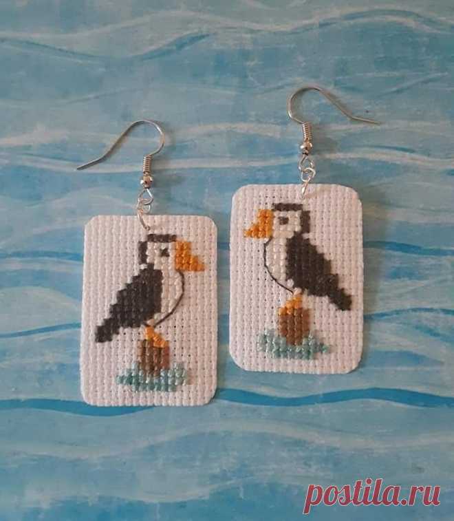 a pair of needled earrings featuring a puffy bird on a white square with blue water in the background