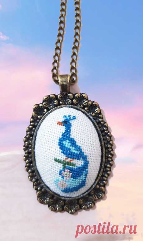 a cross - stitch necklace with a blue bird on it's side and a sky background